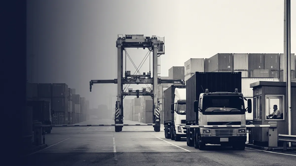 Straddle carrier and trucks at a container terminal gate in fog