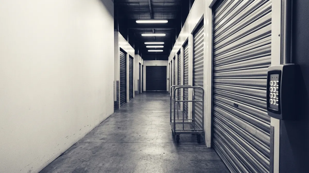 An empty self-storage corridor of roller doors with a trolley left out