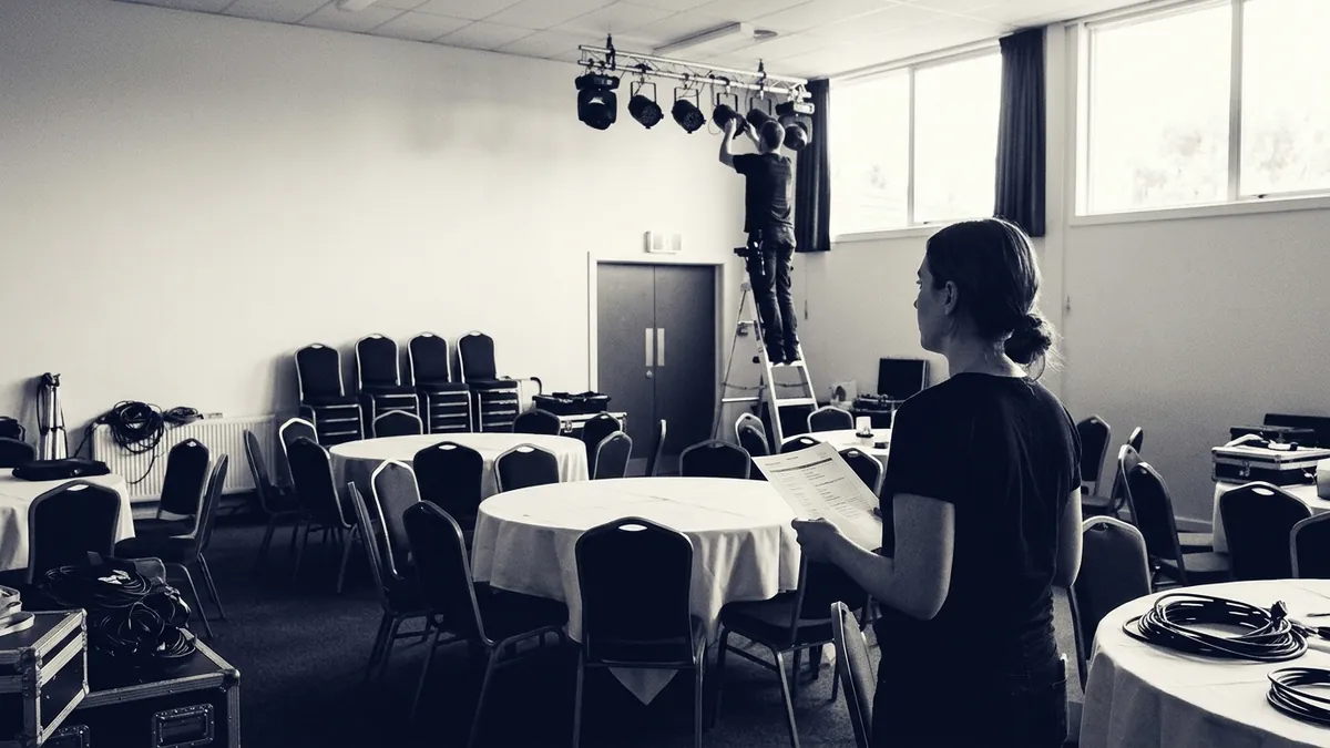 A venue coordinator with a run sheet as a technician rigs lighting over banquet tables