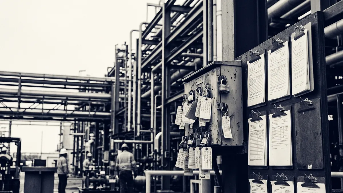 A permit board of isolation tags and clipboards beside process piping on a plant